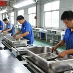 Skilled workers at a stainless steel basin factory assembling high-quality sinks using advanced machinery.